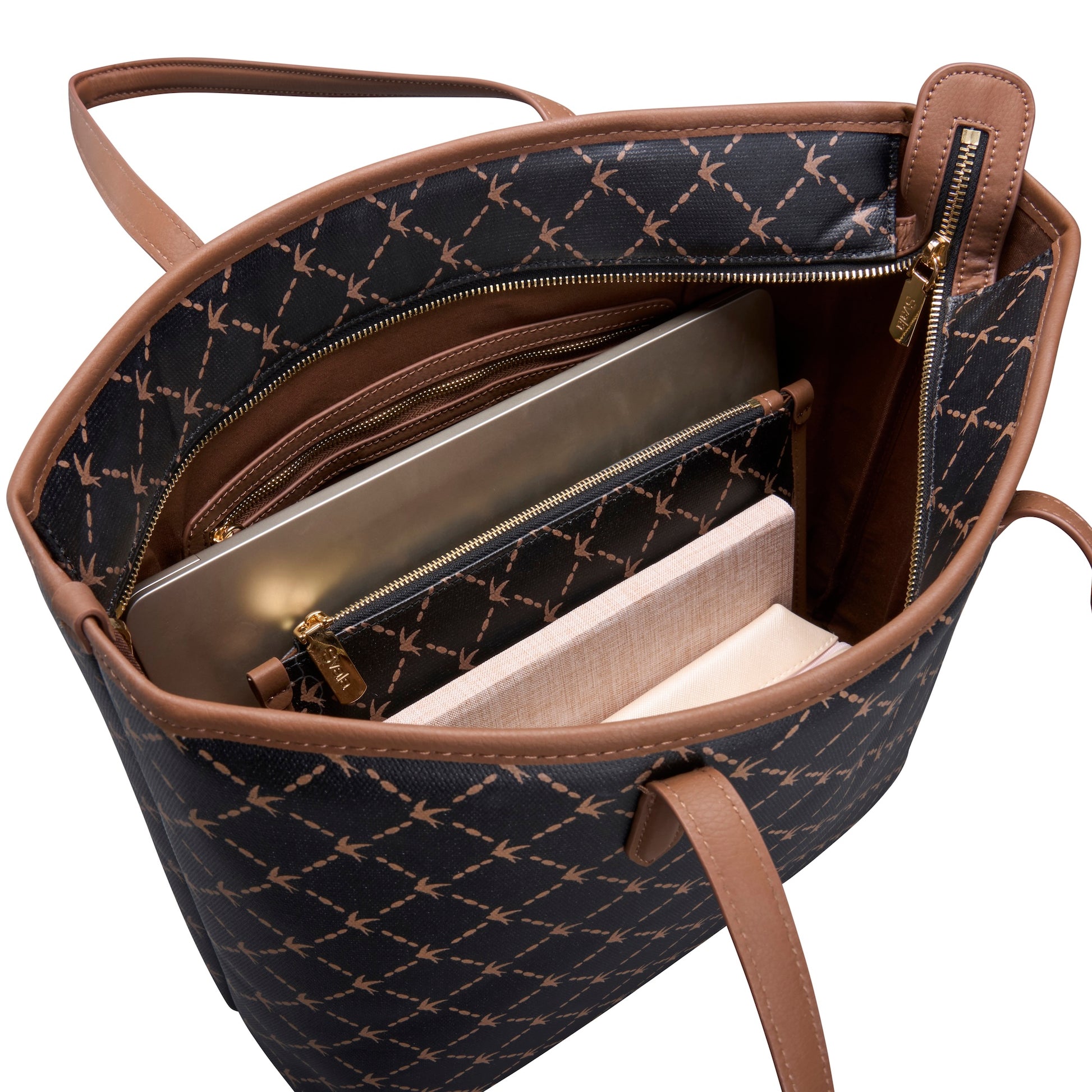 An open tote bag with a black and brown geometric monogram pattern, brown leather handles and trim, and gold-tone zippers. A silver laptop, a light pink notebook, and a white book are partially visible inside the bag against a white background.