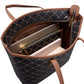 An open tote bag with a black and brown geometric monogram pattern, brown leather handles and trim, and gold-tone zippers. A silver laptop, a light pink notebook, and a white book are partially visible inside the bag against a white background.