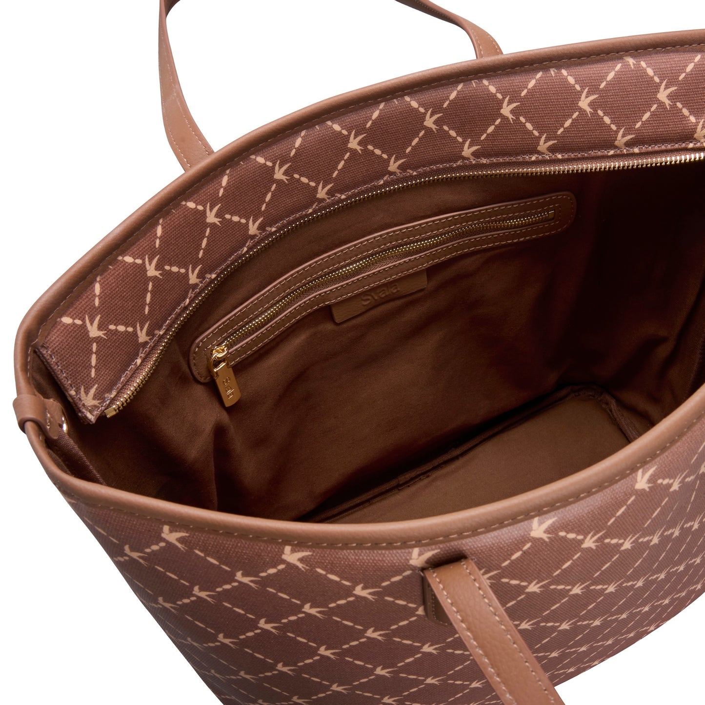Close-up of the interior of a brown tote bag with a beige geometric monogram pattern, showing a zippered pocket and brown handles against a white background.